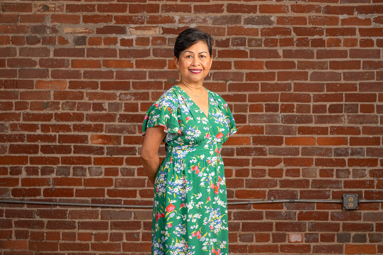 Team member Gloria, standing in front of a red brick wall.